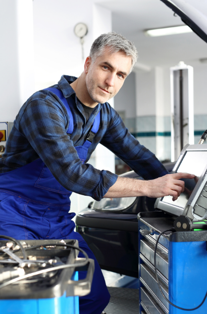 Mechanic in blue overalls using a laptop in an auto repair shop