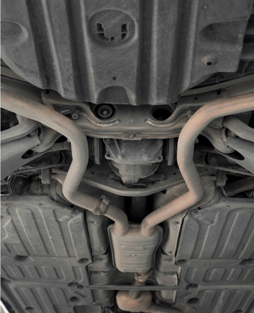 Undercarriage view of a car’s exhaust system and heat shields on a lift