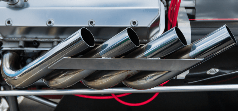 Chrome car exhaust pipes beneath a vehicle, with polished metal tubes and a red cable in the background