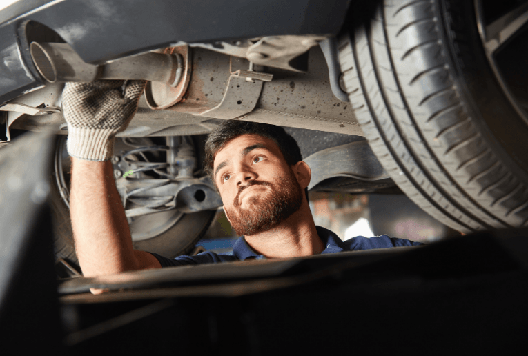 Mechanic inspecting the underside of a car on a lift, wearing gloves and looking upward