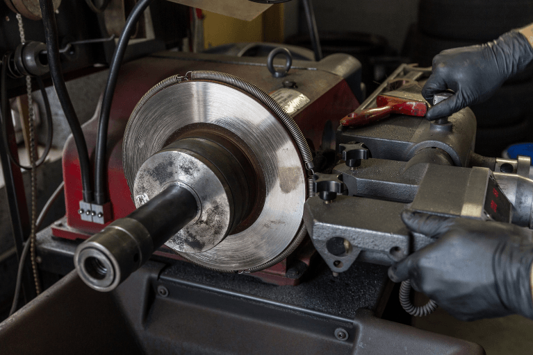 Gloved hands using a lathe to machine a metal disc in a workshop