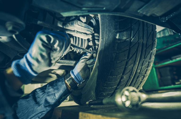Mechanic working under a car, tightening a tire with a wrench in a garage.