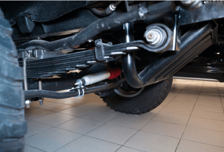 Underbody of a vehicle showing suspension, exhaust, and tire in a garage on tiled floor