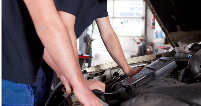 Two people working under the hood of a car in a garage