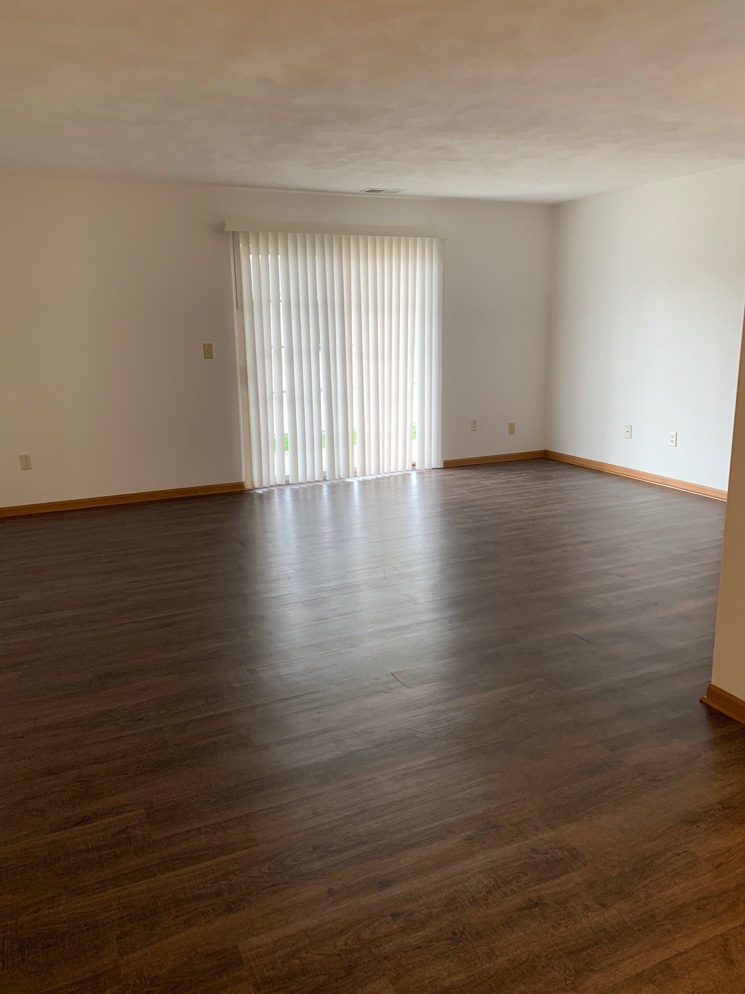 An empty living room with hardwood floors and a sliding glass door.