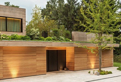 Casa moderna in legno con vegetazione sul tetto e viale d'ingresso alberato.