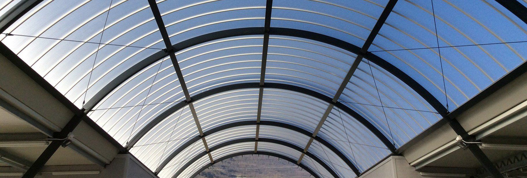 Soffitto con lucernario curvo in vetro e metallo, attraverso il quale si può scorgere il cielo azzurro.