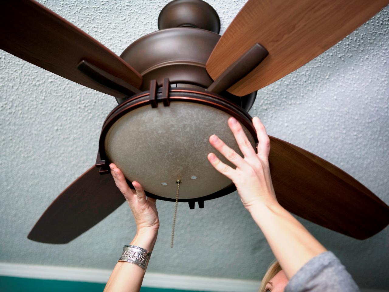 A woman is changing the light on a ceiling fan