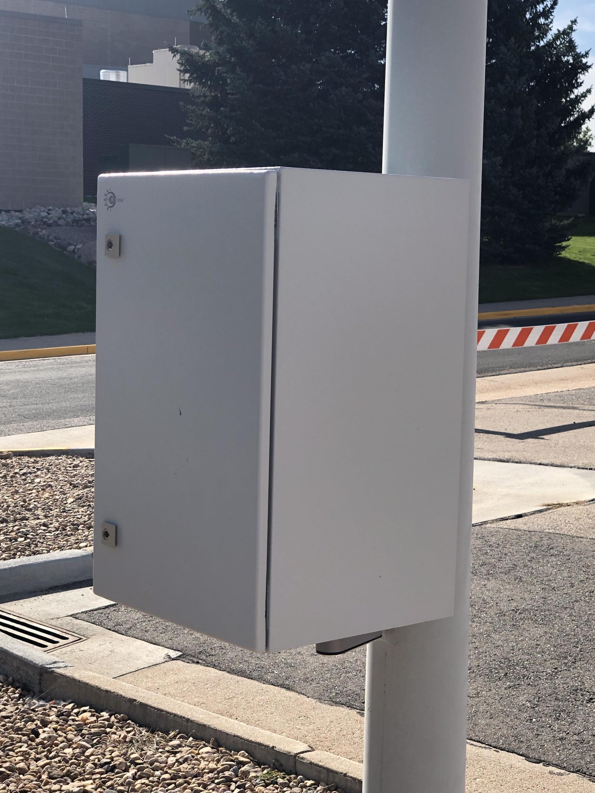 A white box is attached to a pole on the side of the road
