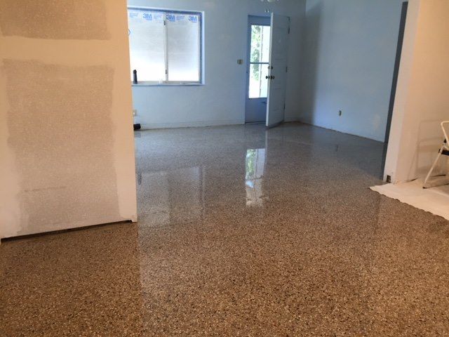 Empty room with speckled floor, white walls, window, and open doorway.