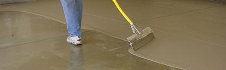 Person using a yellow-handled floor squeegee to spread wet concrete on a smooth floor