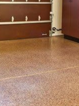Empty garage with speckled tan floor and brown walls, showing wall shelves in the background