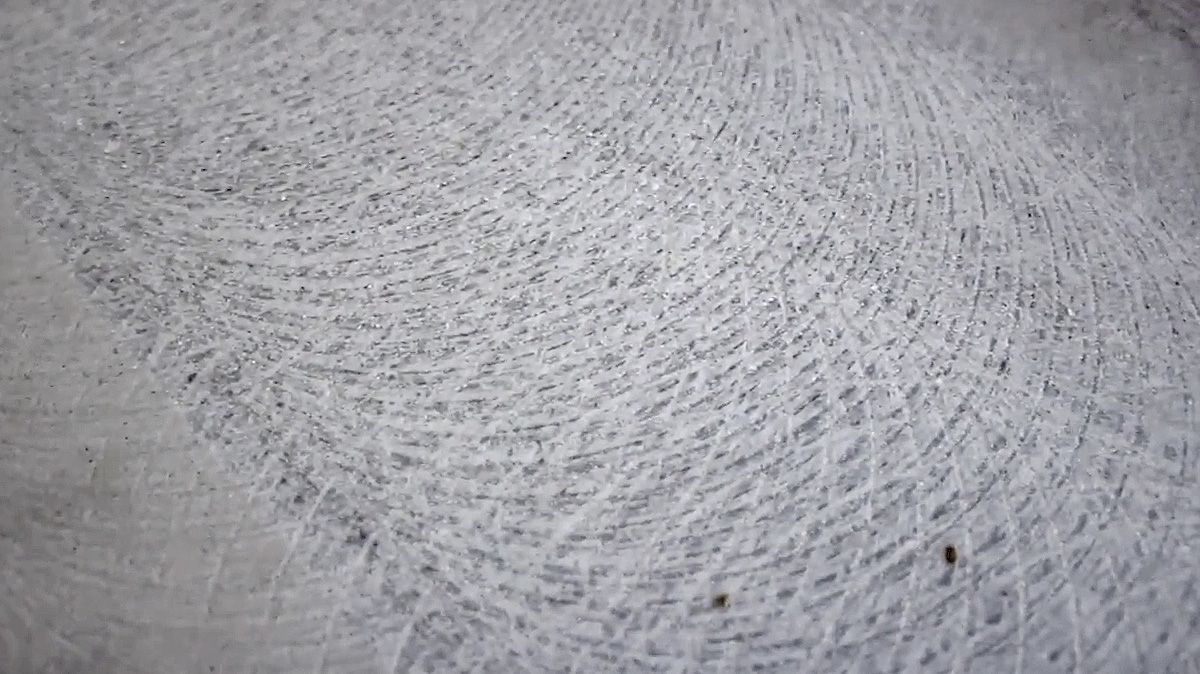 Close-up of a white textured surface with curved brush-like patterns and small dark specks