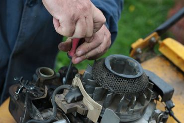 a man is fixing a lawn mower with a screwdriver .