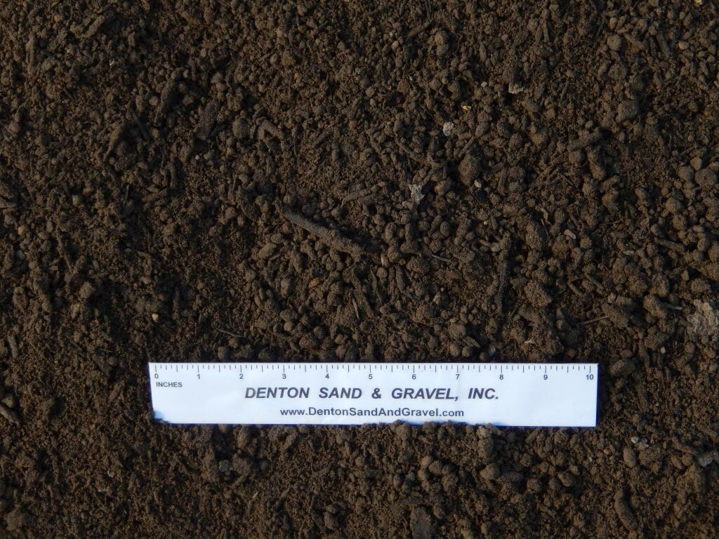 Dark brown soil with a white ruler from Denton Sand & Gravel.