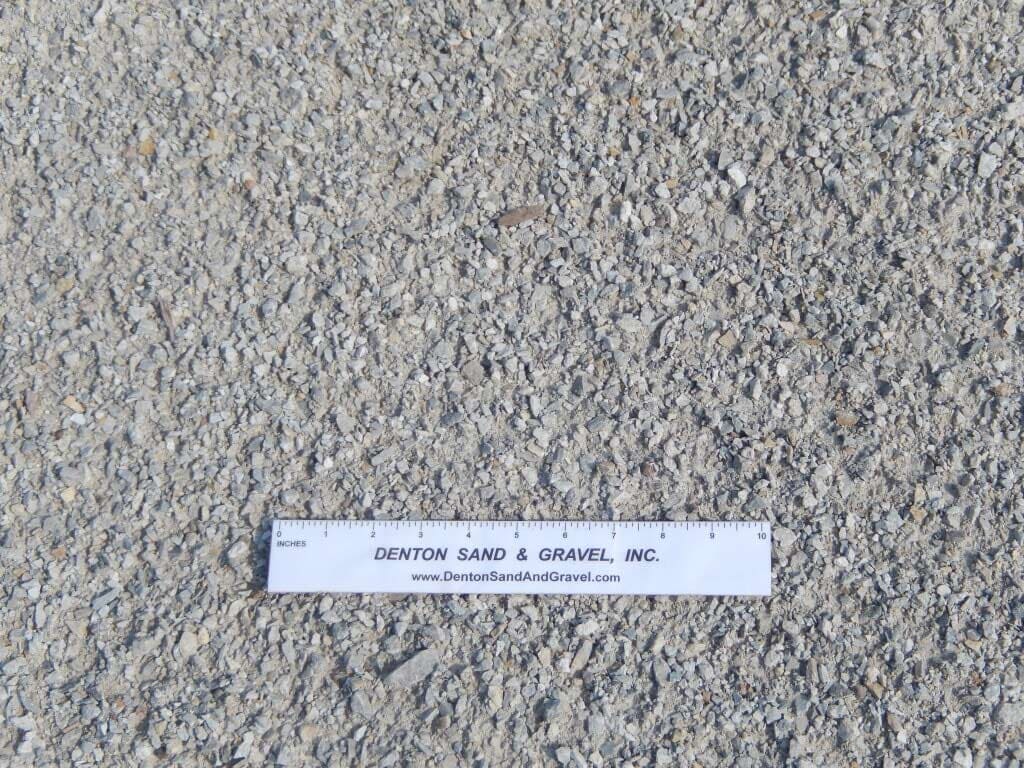 Close-up of gravel, mostly light grey, with a ruler from Denton Land & Gravel.