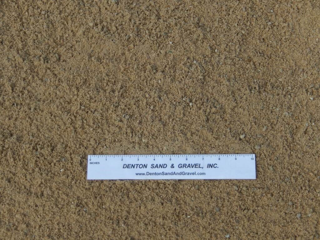 Close-up view of tan sand with a ruler showing grain size.