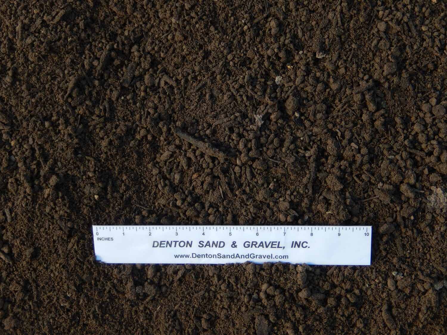 Dark brown soil with a white ruler from Denton Sand & Gravel.