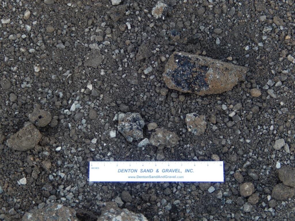 Close-up of gravel and small rocks, with a ruler for scale. The largest rock has a dark center.