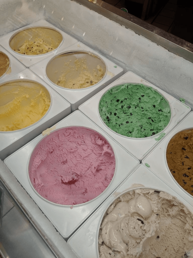 A high-angle view of multiple circular tubs of colorful ice cream flavors arranged in a display freezer.