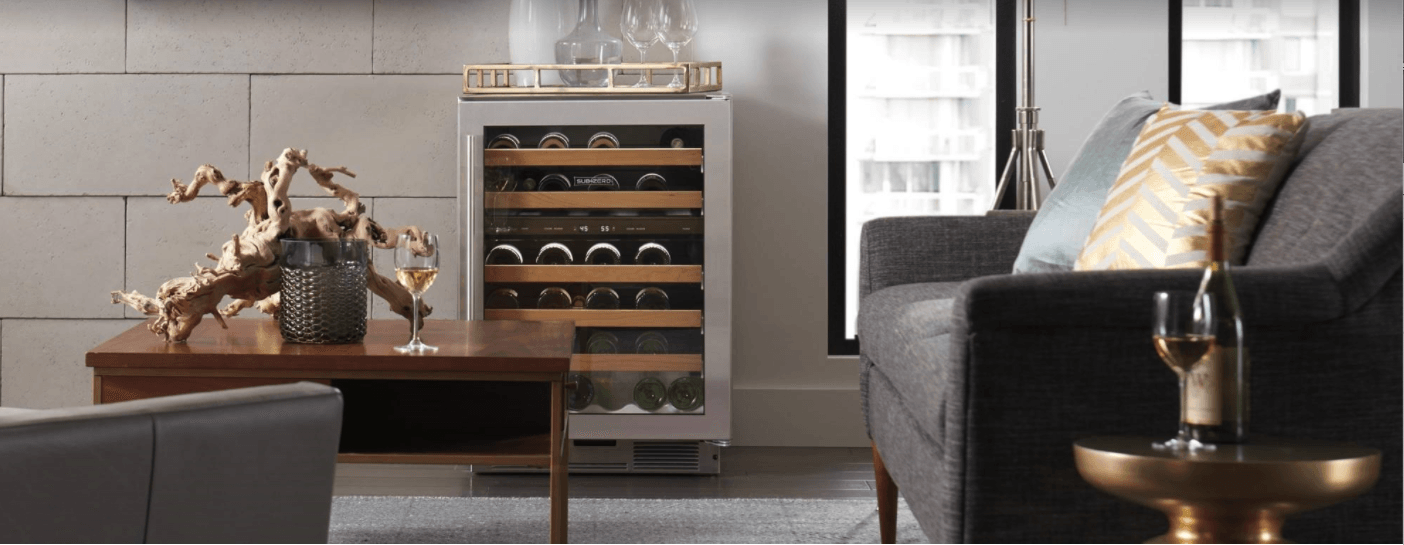 A modern living room features a wine cooler next to a couch with a coffee table holding wine glasses and decorative art.