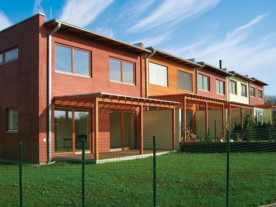 Row of townhouses, each with a different colored brick facade and wooden patio covers, on a green lawn.