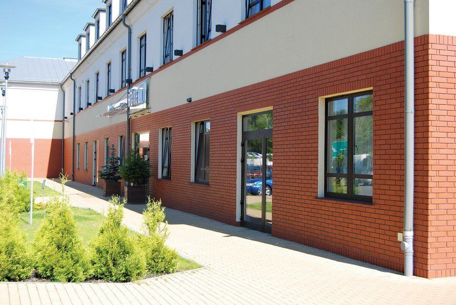 Red brick building exterior with windows and a paved walkway.