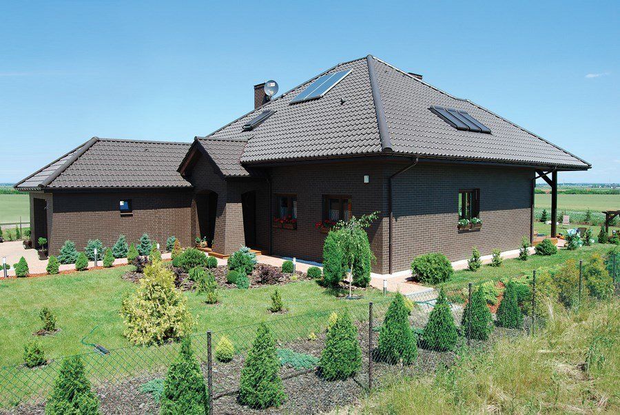 Brown house with a matching garage and landscaped yard, blue sky.