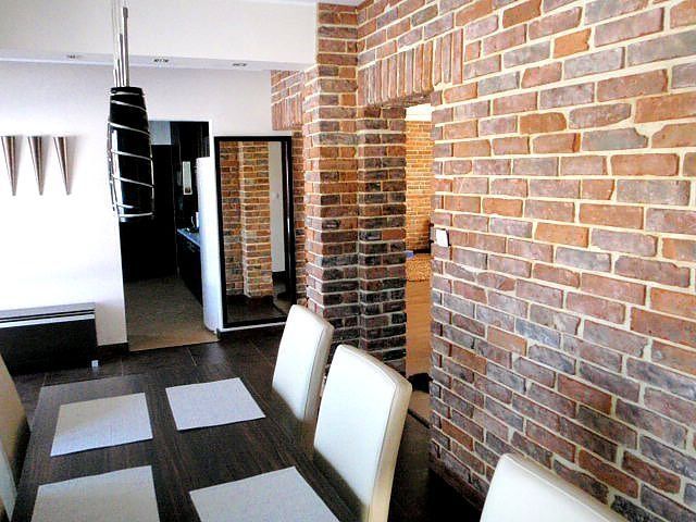 Dining room with brick wall, table with white chairs, dark wood floor, and decorative lighting.