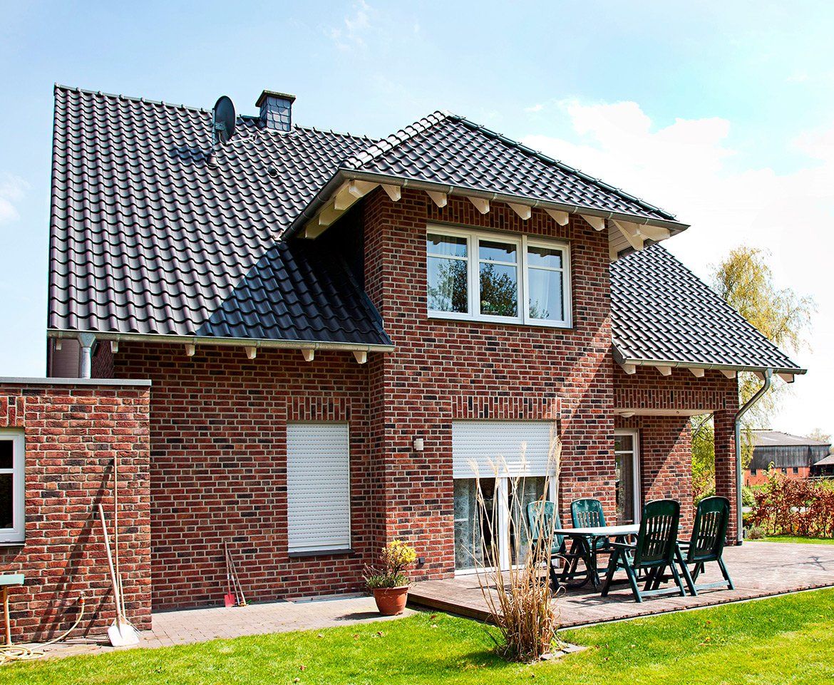Brick house with a tiled roof, white window frames, and patio furniture on a sunny day.