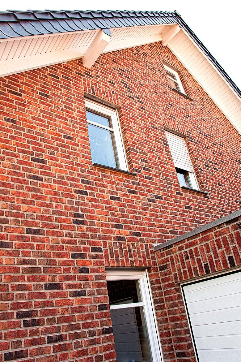 Brick house exterior with three windows, a garage door, and a dark roof.