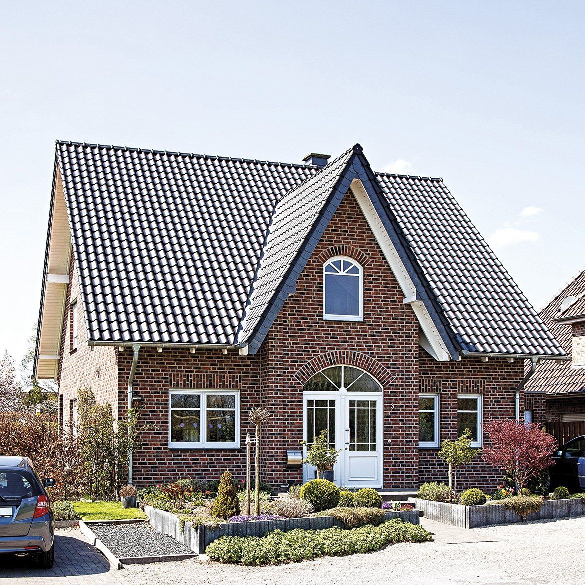 Brick house with dark tiled roof, white trim, arched doorway, and small garden.