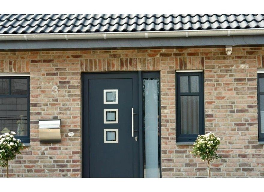 Brick facade with dark blue door, sidelight, and windows. Roof is dark tile.