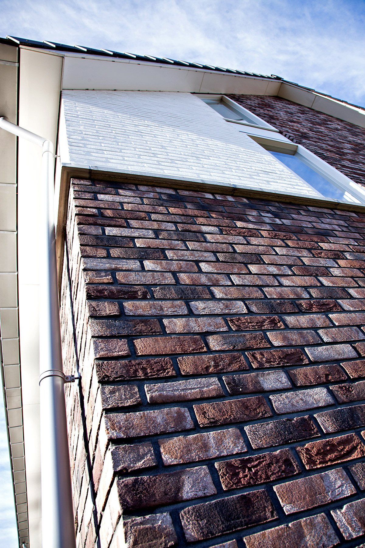 Brick exterior of a building with a white upper section and a gutter along the side.