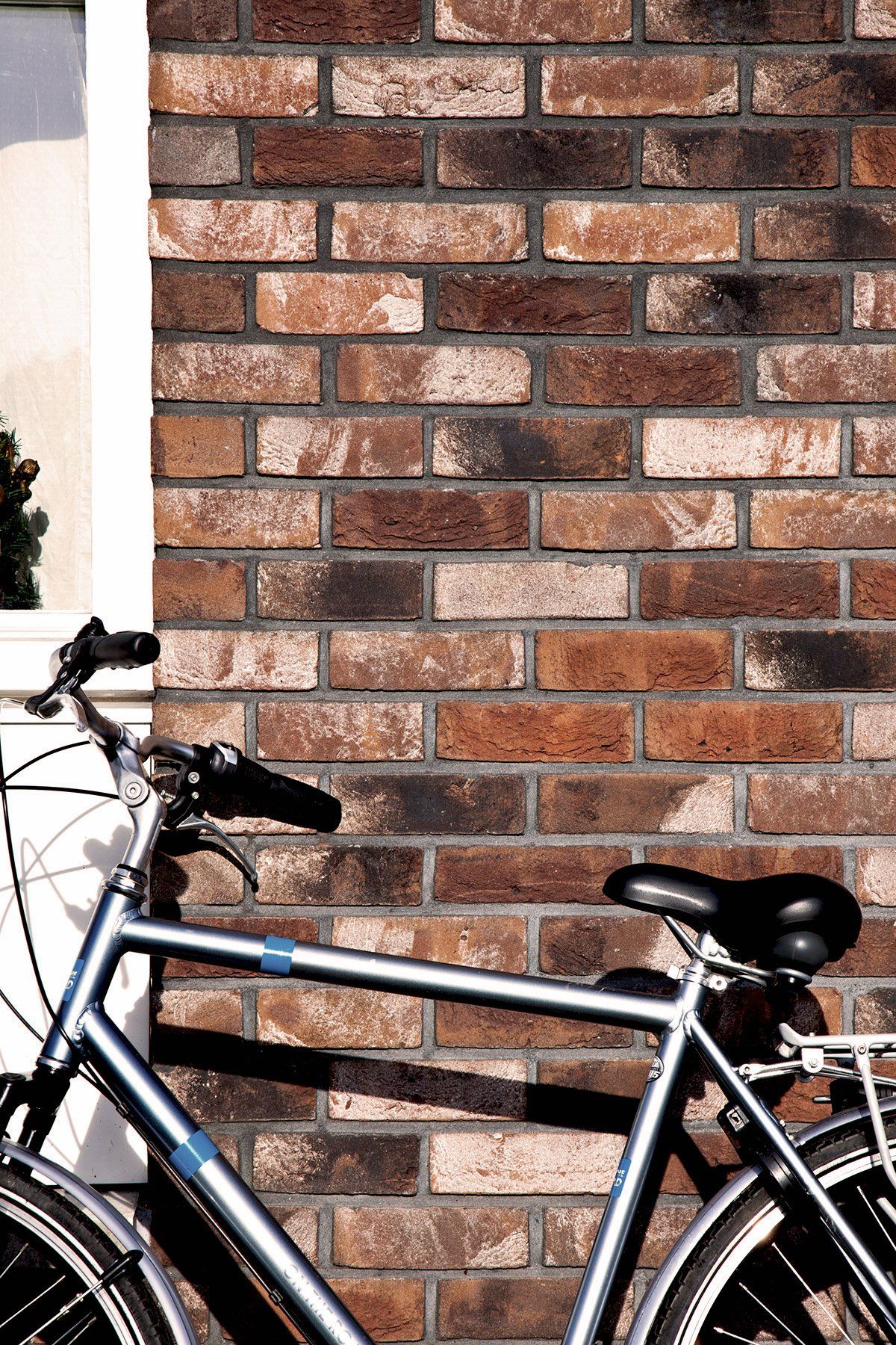 Silver bicycle leaning against a brick wall next to a window.