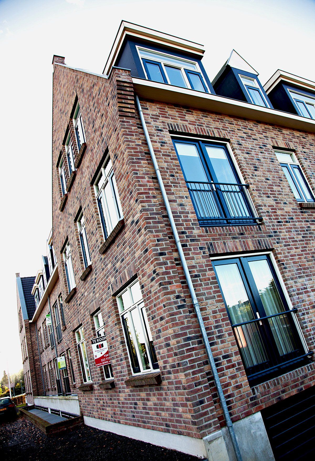 Brick building with multiple windows; dormers on top floor.