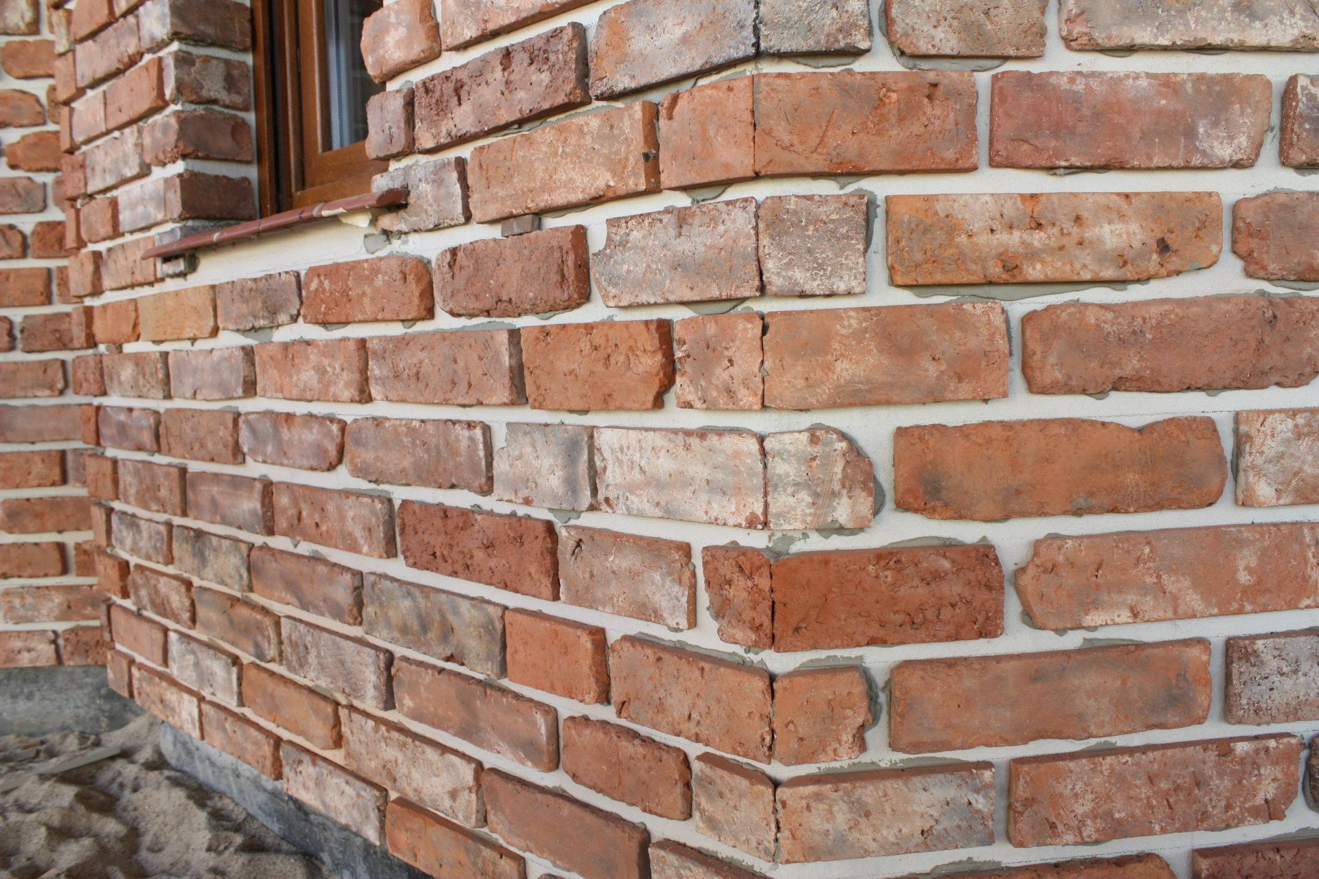 Brick wall corner with red-brown bricks and white mortar, near a window frame.