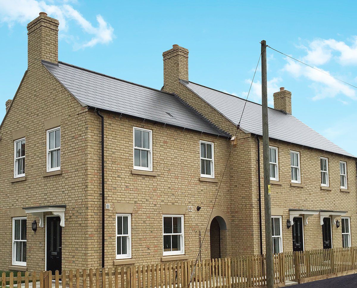 Row of brick townhouses with white windows, black doors, and a wooden fence under a blue sky.