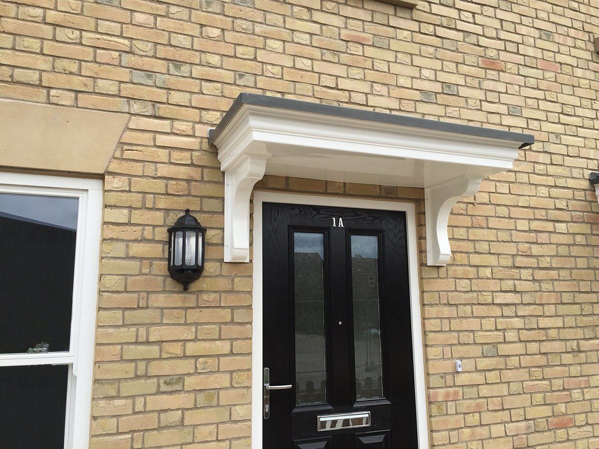 Black door with white canopy, brick facade, and a black sconce.