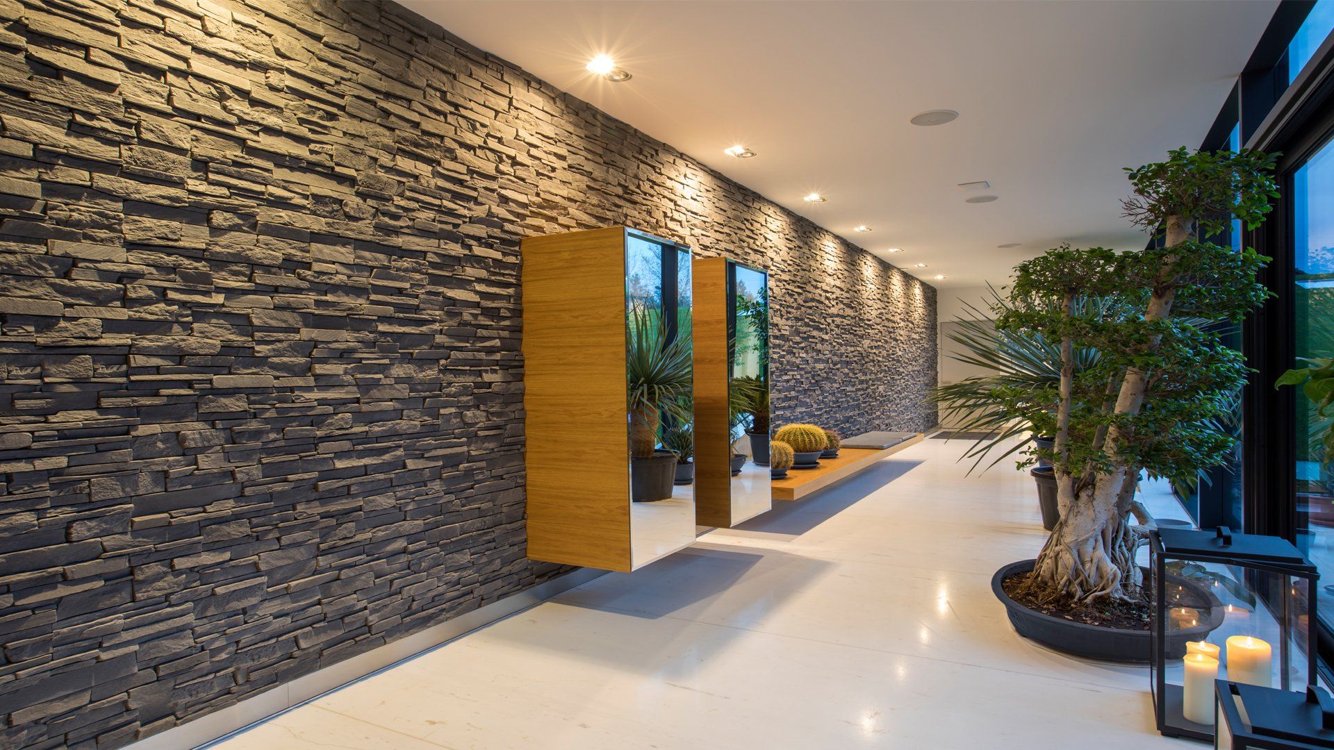 Hallway with dark stone wall, white floor, large mirrors, and plants.