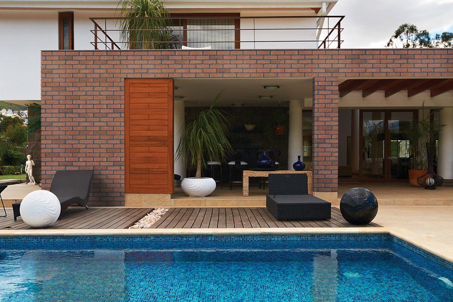 Poolside view of a modern house with a pool, brick wall, and outdoor seating.