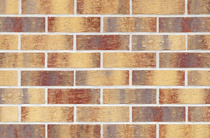 Brick wall with alternating rows of light yellow, reddish-brown, and gray bricks, separated by white mortar.