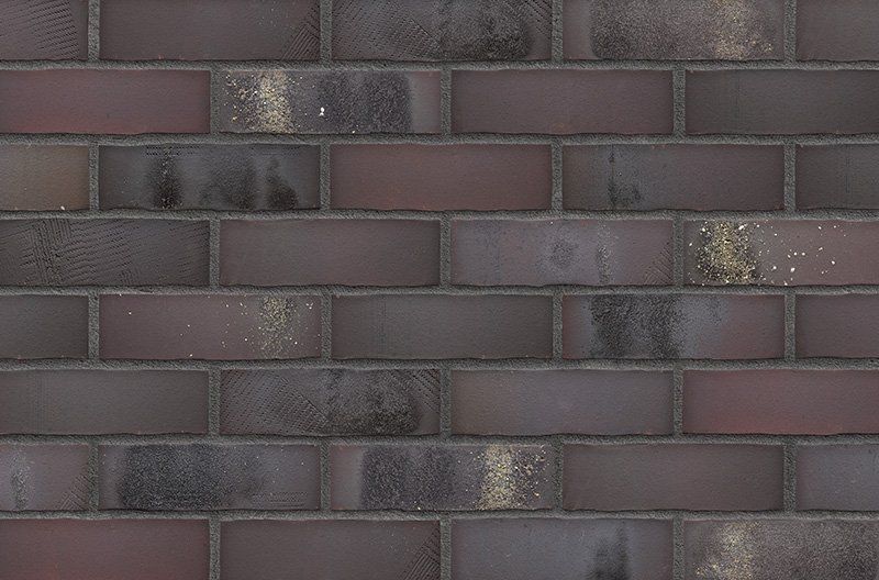 Dark brown brick wall, with mortar joints and patches of discoloration.