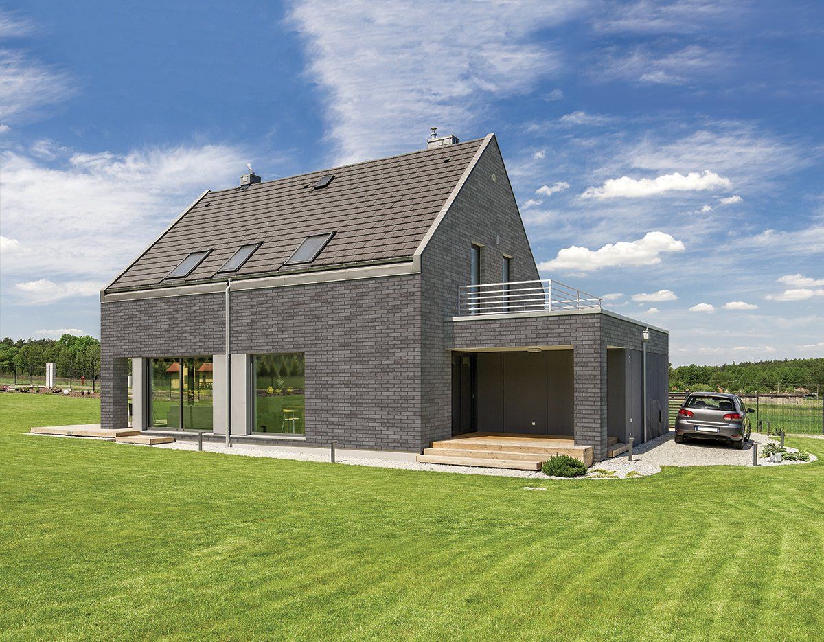 Modern house with grey brick facade, carport, and green lawn under a blue sky.