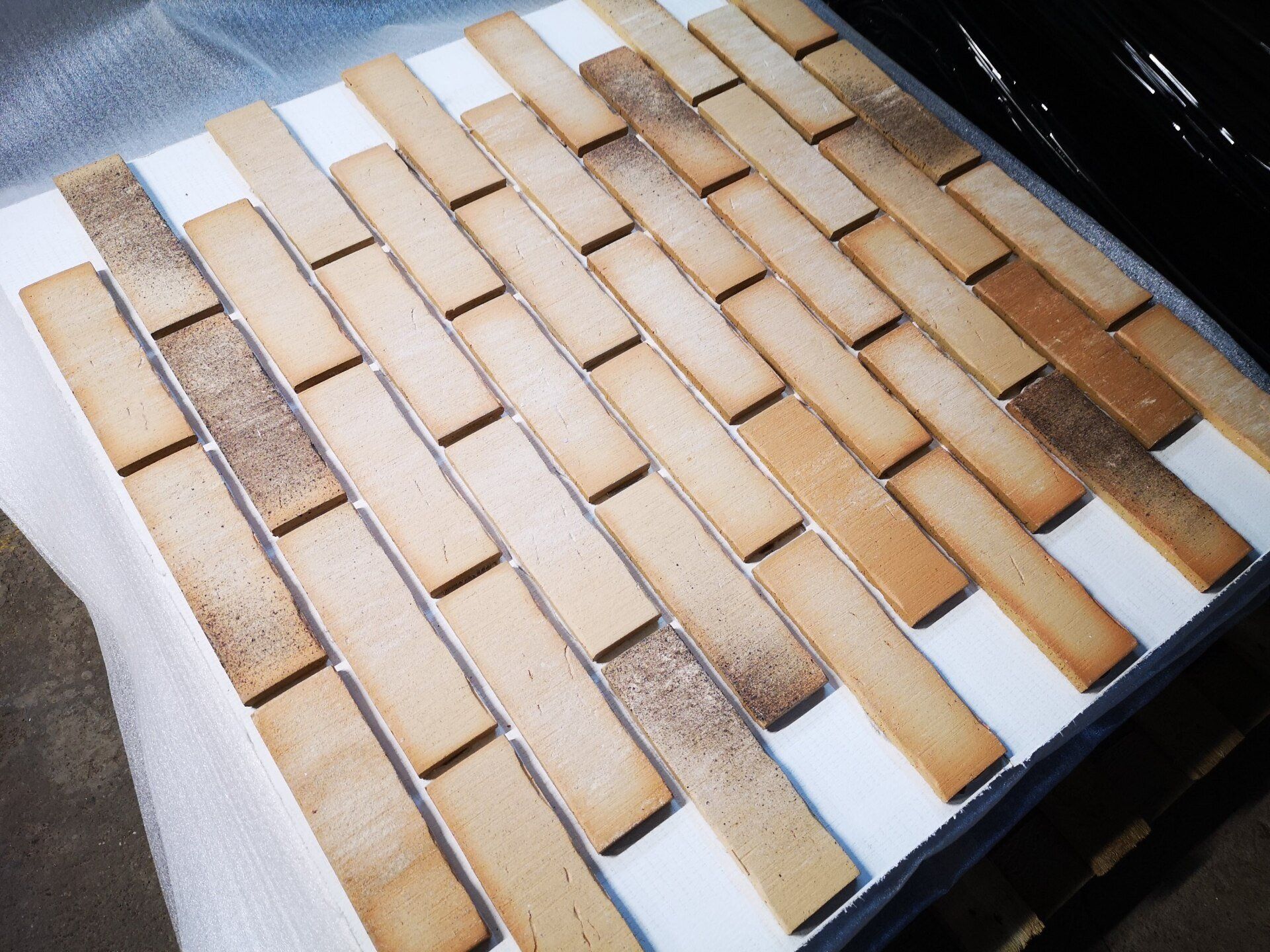 Brick tiles arranged in a diagonal pattern on a white surface, varying in tan color with some darker patches.