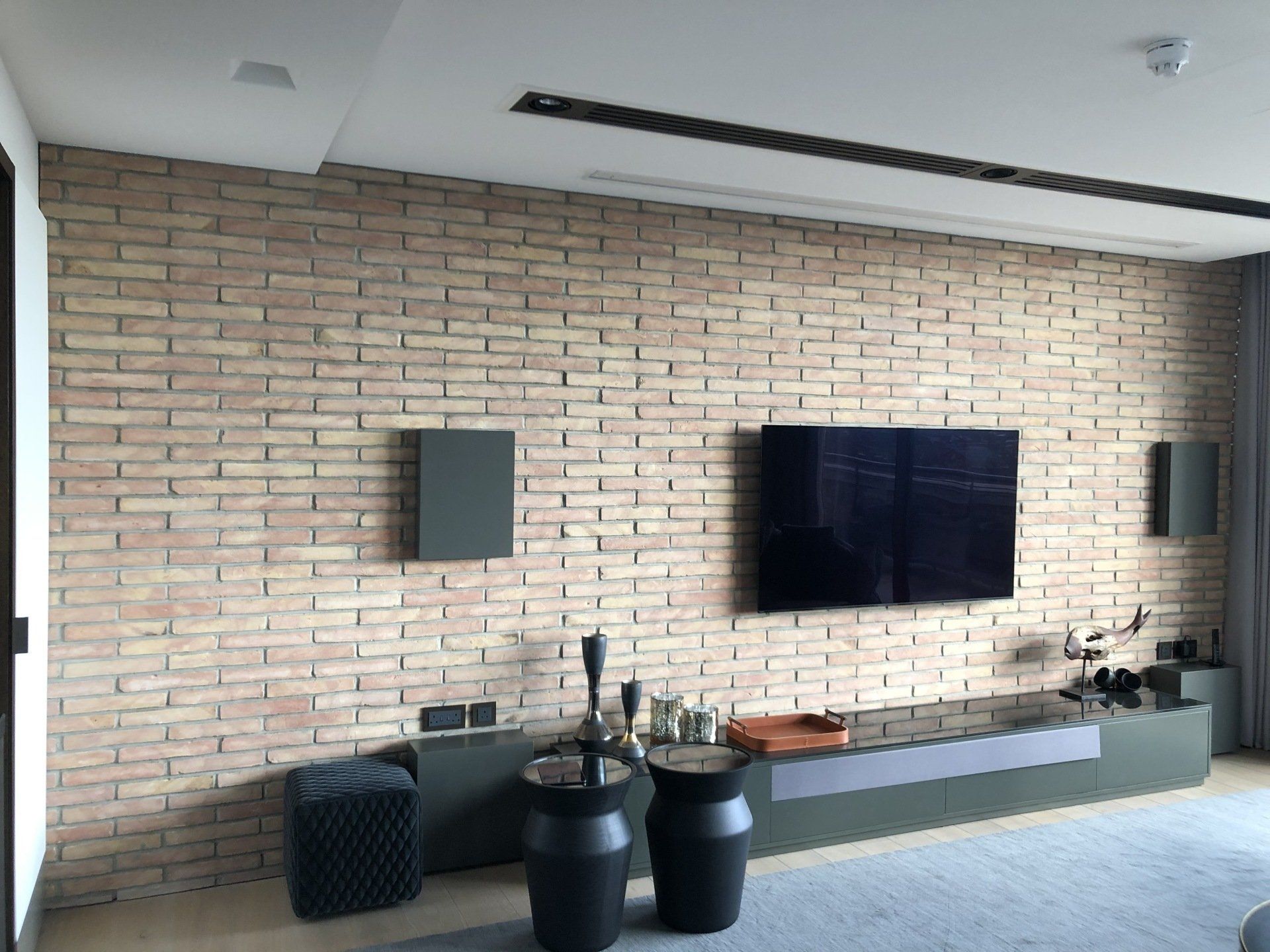 Living room with brick accent wall, TV, and speakers. Gray and black furniture.