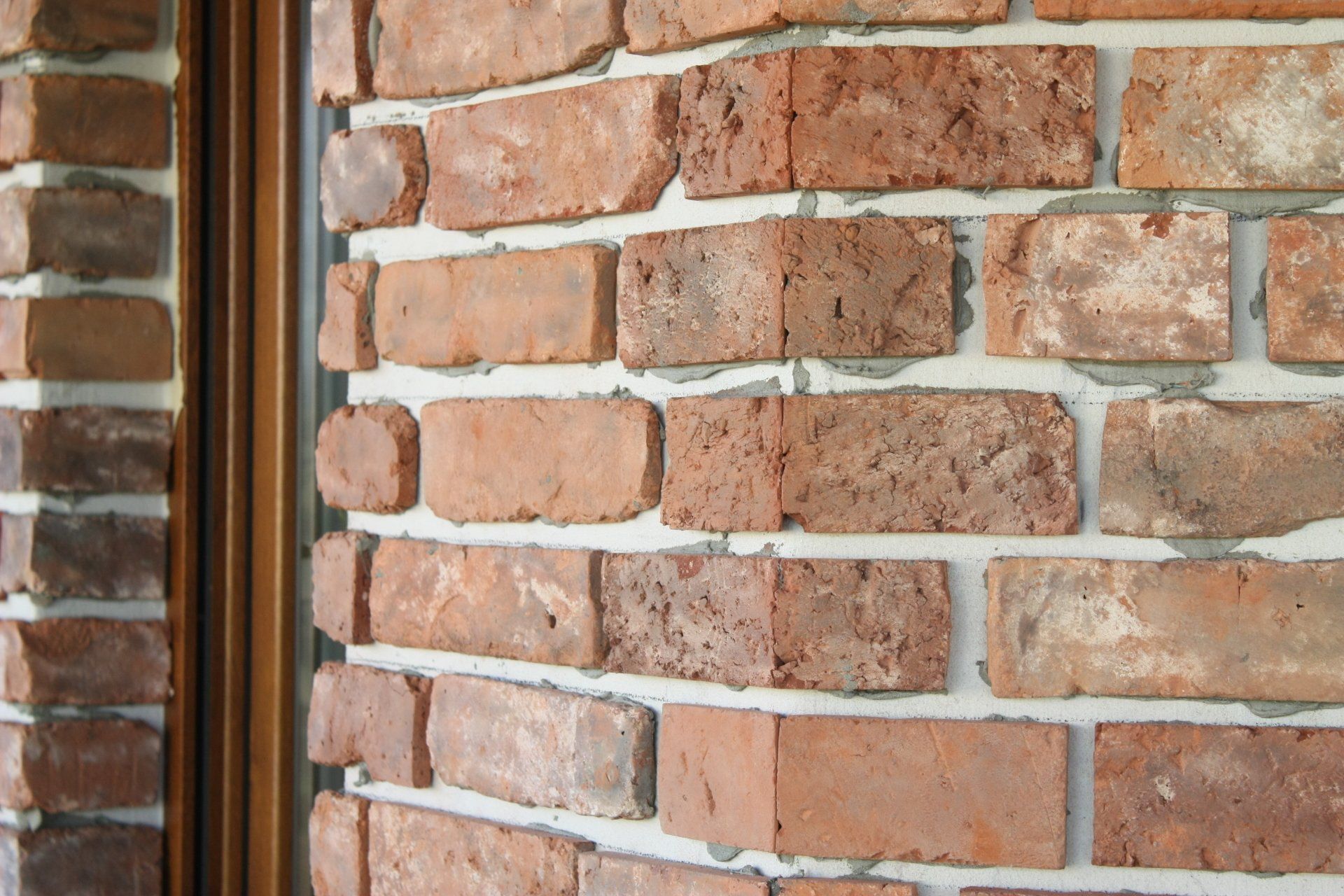Close-up of a brick wall with red-brown bricks and white mortar, next to a brown-framed mirror.