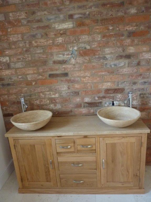 Wooden double vanity with two bowl sinks against a brick wall.
