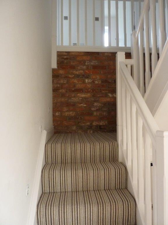 Staircase with striped carpet, white railing, brick wall at top.