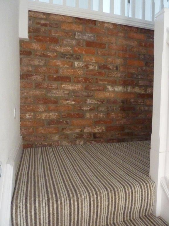 Stairway with striped carpet, brick wall, and white trim.